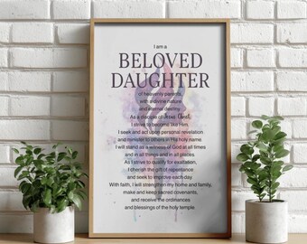Könnte beinhalten: Gerahmter Druck mit dem Text "I am a BELOVED DAUGHTER" in einer dekorativen Schriftart. Der Druck hat einen Hintergrund im Aquarellstil und einen Holzrahmen. Zwei kleine Topfpflanzen flankieren den gerahmten Druck.