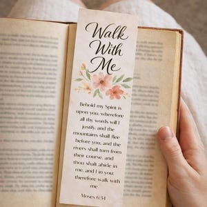 May include: A bookmark with the text "Walk With Me" and a floral design is placed in an open book. The bookmark features a quote from Moses 6:34. The book has aged, yellowed pages.