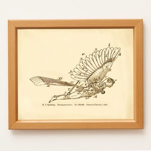 May include: Framed vintage print of a flying machine patent illustration. The sepia-toned artwork features a detailed diagram of a winged apparatus with a human figure, labeled with letters. The wooden frame adds a classic touch.