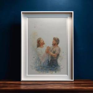 May include: Framed watercolour painting showing two figures in water. One wears a white robe, the other a tan tunic. The artwork is displayed on a dark wood surface against a dark blue wall.