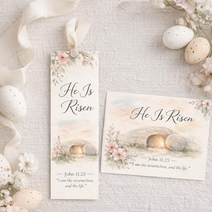 May include: A bookmark and card set with the text "He Is Risen" and a watercolor illustration of an empty tomb. The bookmark has a ribbon and floral accents. The card and bookmark include the Bible verse John 11:25.