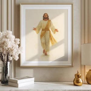 May include: A framed print depicts a figure in flowing white and gold robes, arms outstretched. The artwork is set against a soft, neutral background, framed in gold. The image is displayed on a white marble surface.