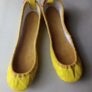 May include: A pair of yellow leather ballet flats with a white lining and pink laces.