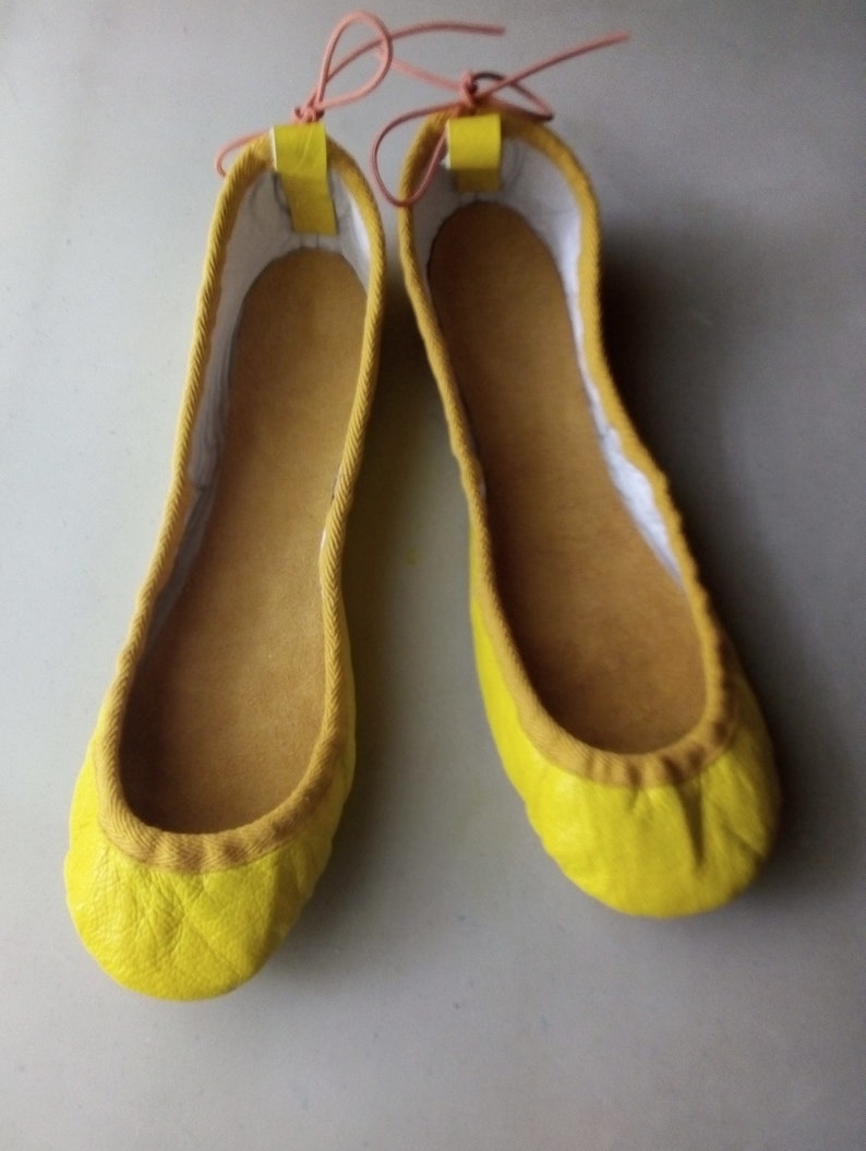 May include: A pair of yellow leather ballet flats with a white lining and pink laces.