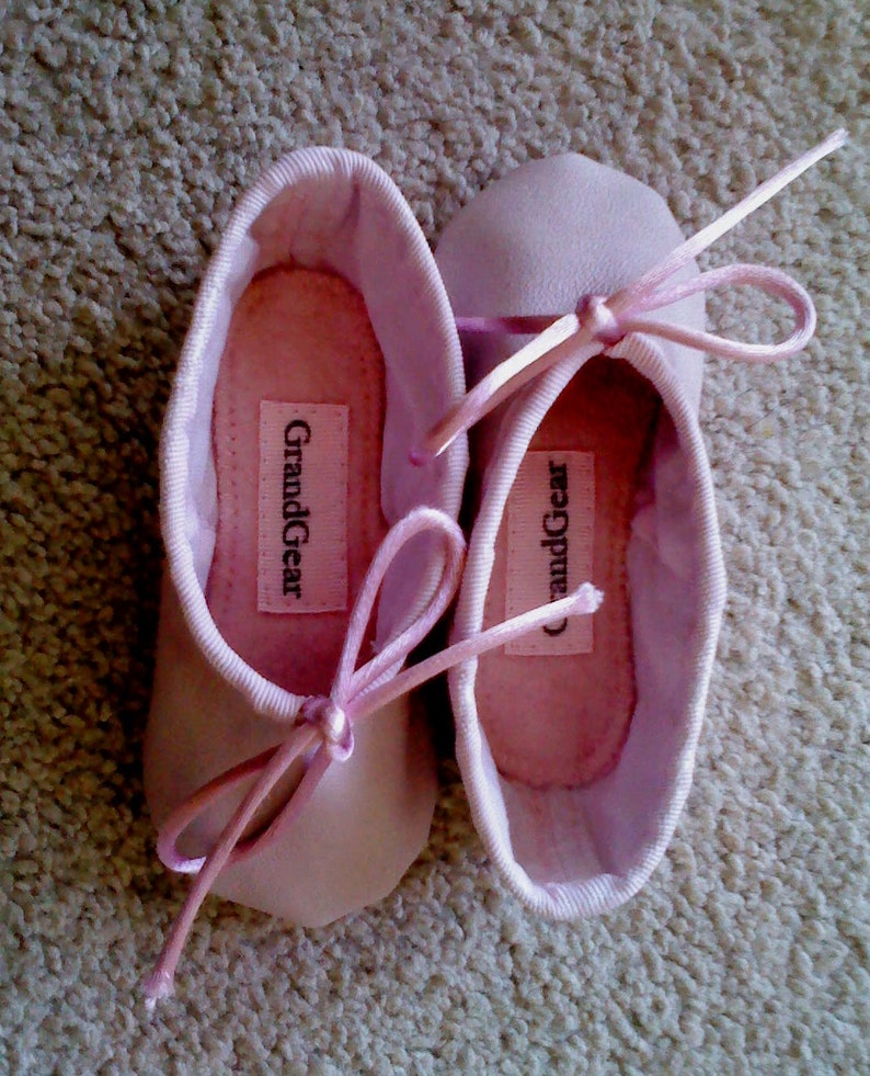 May include: A pair of pink ballet slippers with satin ribbons. The slippers have the brand name "GrandGear" printed on the inside.