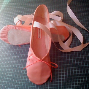 May include: A pair of pink satin ballet shoes with white ribbons. The shoes have a label that says "GrandGear".