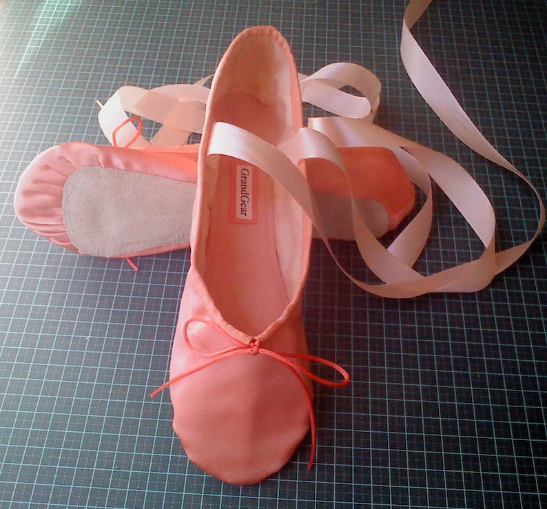 May include: A pair of pink satin ballet shoes with white ribbons. The shoes have a label that says "GrandGear".