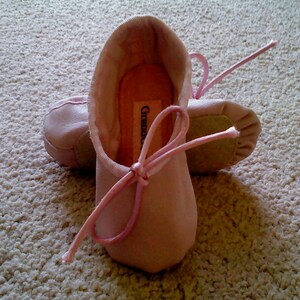 May include: A pair of pink ballet slippers with a pink ribbon tied around the front. The slippers have the word "Grazie" written on the inside.