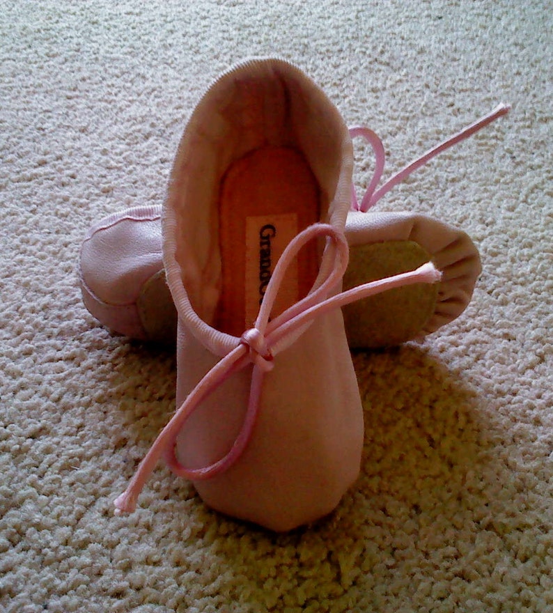 May include: A pair of pink ballet slippers with a pink ribbon tied around the front. The slippers have the word "Grazie" written on the inside.
