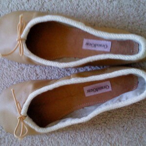 May include: A pair of beige ballet flats with white trim and a bow on the toe. The flats have the brand name "Grand Gear" printed on the insole.