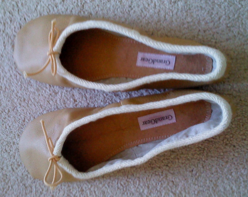 May include: A pair of beige ballet flats with white trim and a bow on the toe. The flats have the brand name "Grand Gear" printed on the insole.