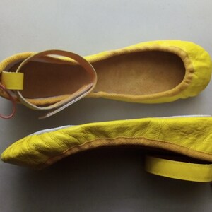 May include: A pair of yellow leather ballet flats with a strap and bow detail. The flats have a pointed toe and a low heel.