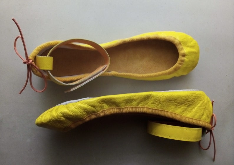 May include: A pair of yellow leather ballet flats with a strap and bow detail. The flats have a pointed toe and a low heel.