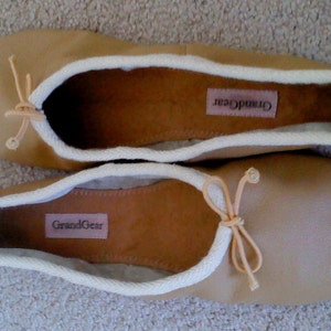 May include: A pair of tan leather ballet flats with white trim and a bow on the toe. The flats have the brand name "GrandGear" printed on the inside.