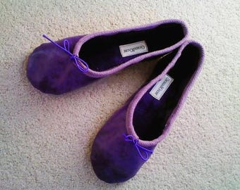 May include: Two purple ballet slippers with a purple ribbon bow on each. The slippers have the text "Charmed" on the sole.