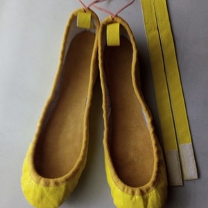 May include: Two yellow fabric ballet flats with a pair of yellow fabric ties.