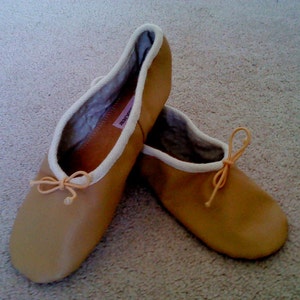 May include: A pair of tan leather ballet slippers with white trim and a light pink ribbon tied at the toe.