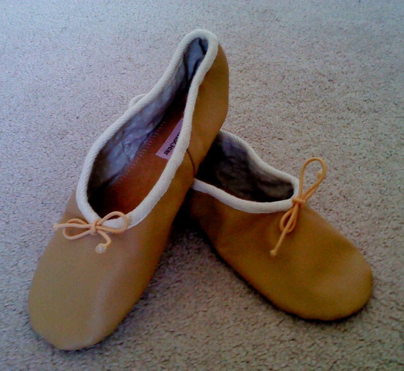 May include: A pair of tan leather ballet slippers with white trim and a light pink ribbon tied at the toe.