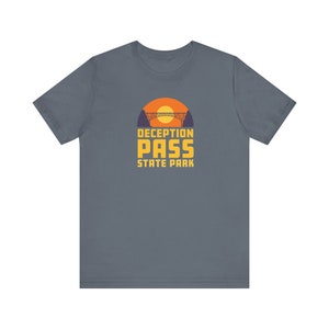 May include: A dark blue t-shirt with a yellow graphic of a bridge and sunset. The text "DECEPTION PASS STATE PARK" is printed in yellow below the graphic.