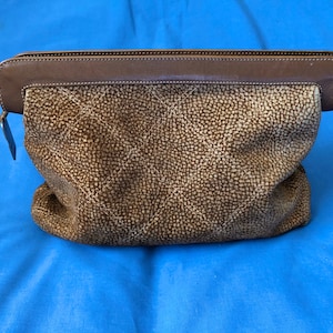 May include: A brown leather zippered pouch with a textured, quilted pattern. The pouch has a brown leather trim around the top edge.
