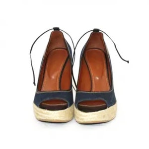 May include: A pair of blue denim wedge sandals with a peep toe and a brown leather insole. The sandals have a tied ankle strap.