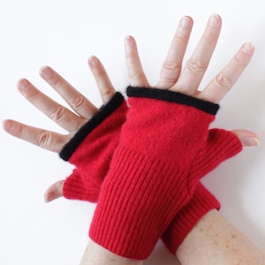 May include: Red fingerless gloves with a black trim. The gloves are made of a ribbed knit material. The gloves are shown on a white background.