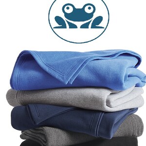 May include: A stack of five fleece blankets in various shades of blue and gray. The top blanket is a bright blue, followed by a light gray, a dark blue, a medium gray, and a black blanket. A frog logo is visible in the top left corner of the image.
