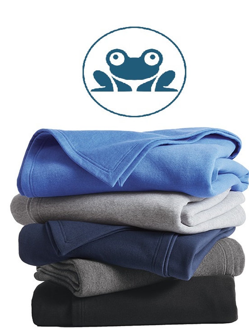 May include: A stack of five fleece blankets in various shades of blue and gray. The top blanket is a bright blue, followed by a light gray, a dark blue, a medium gray, and a black blanket. A frog logo is visible in the top left corner of the image.