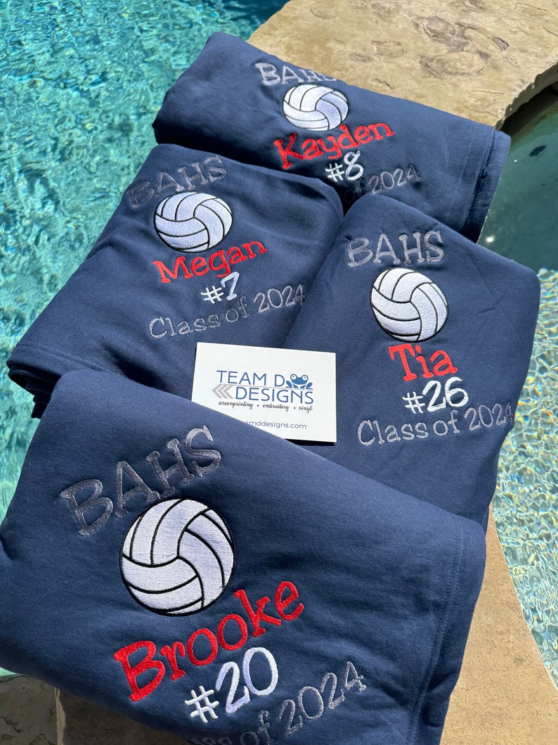 May include: Four navy blue fleece blankets with embroidered volleyball designs. Each blanket features a volleyball, a name, a number, and the text "BAHS" and "Class of 2024".