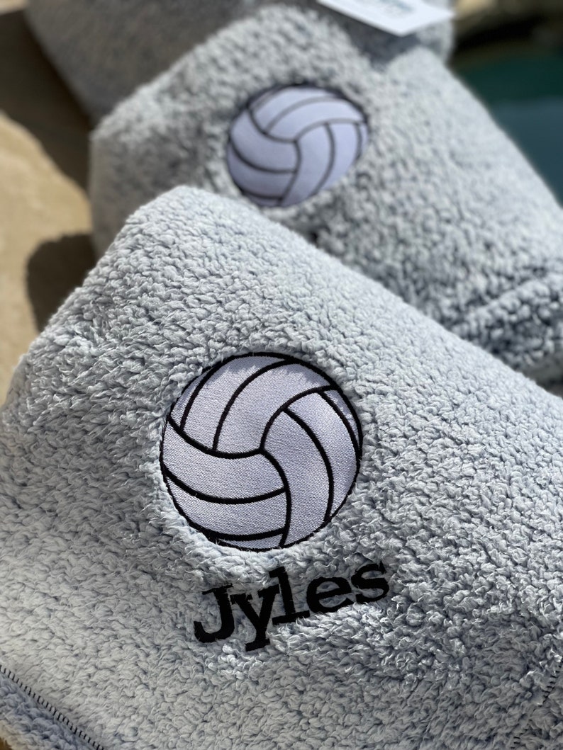 May include: A gray, fuzzy towel with a white volleyball and the name "Jyles" embroidered in black.