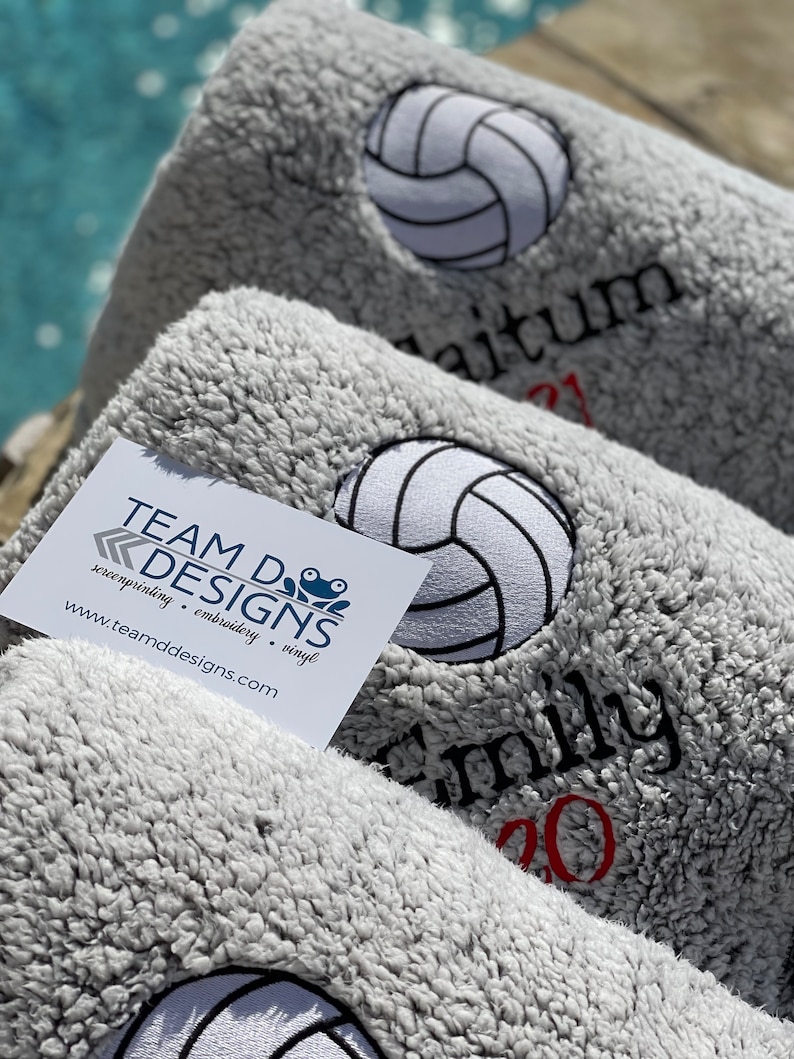 May include: Three gray fleece blankets with embroidered volleyball designs. The blankets have the text "Team D Designs", "Emily 2020", and "Dalton 21" on them.