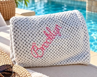 May include: A folded light gray waffle-knit blanket featuring the name Brooklyn embroidered in bright pink cursive script across the center. The textured fabric has a raised, grid-like pattern throughout the surface of the material.