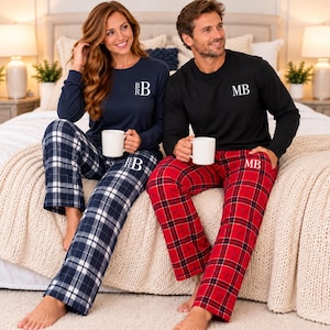 May include: Two sets of long-sleeve pajamas. One set features a navy blue top with white monogram BR and navy plaid pants. The other set features a black top with white monogram MB and red plaid pants. Both include white mugs.
