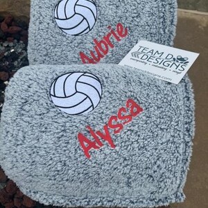 May include: Two gray fleece blankets with embroidered volleyball designs and names. The top blanket has the name "Aubrie" and the bottom blanket has the name "Alyssa".