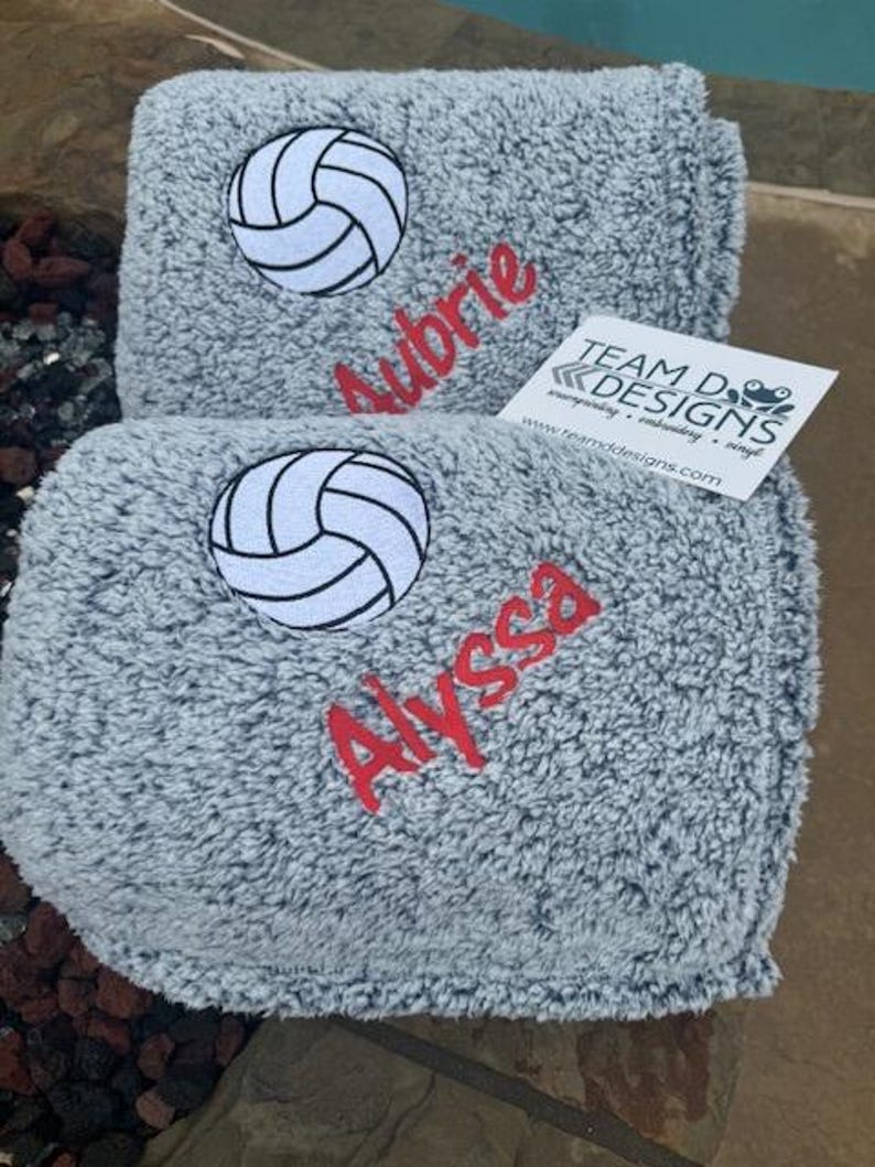 May include: Two gray fleece blankets with embroidered volleyball designs and names. The top blanket has the name "Aubrie" and the bottom blanket has the name "Alyssa".