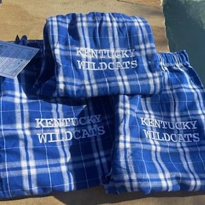 May include: Three pairs of blue and white plaid pajama pants with the embroidered text "Kentucky Wildcats" on each pair.