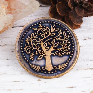 May include: A round, gold-toned metal pin with a blue background and a detailed, gold-coloured tree design.