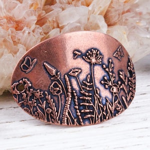 May include: A copper charm with an embossed design of wildflowers and butterflies. The charm is oval shaped and has a rustic, hand-crafted look.