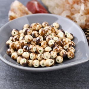 May include: A bowl of brown and white ceramic beads. The beads are round and have a speckled pattern.