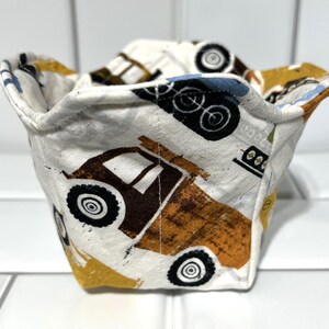 May include: A white fabric bowl with a construction vehicle print. The bowl features yellow, brown, and blue trucks on a white background.