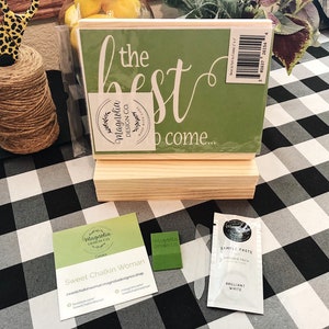 May include: A green wooden sign with the text "the best to come..." in white lettering. The sign is on a wooden stand and has a Magnolia Design Co. logo. There is a business card for Sweet Chalkin Woman and a sample of white chalk paste.
