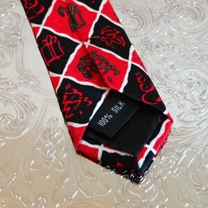 May include: A red and black silk tie with a diamond pattern and a white tag that says "100% Silk".