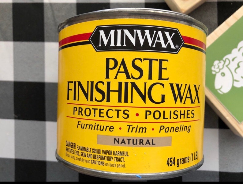 May include: A yellow can of Minwax Paste Finishing Wax. The can is labeled "Protects &bull; Polishes" and lists "Furniture &bull; Trim &bull; Paneling". The can is labeled "Natural" and has a warning label that reads "DANGER! FLAMMABLE SOLID! VAPOR HARMFUL. IRRITATES EYES, SKIN AND RESPIRATORY TRACT. Before using, carefully read CAUTIONS on back panel." The can is labeled "454 grams (1 LB)".