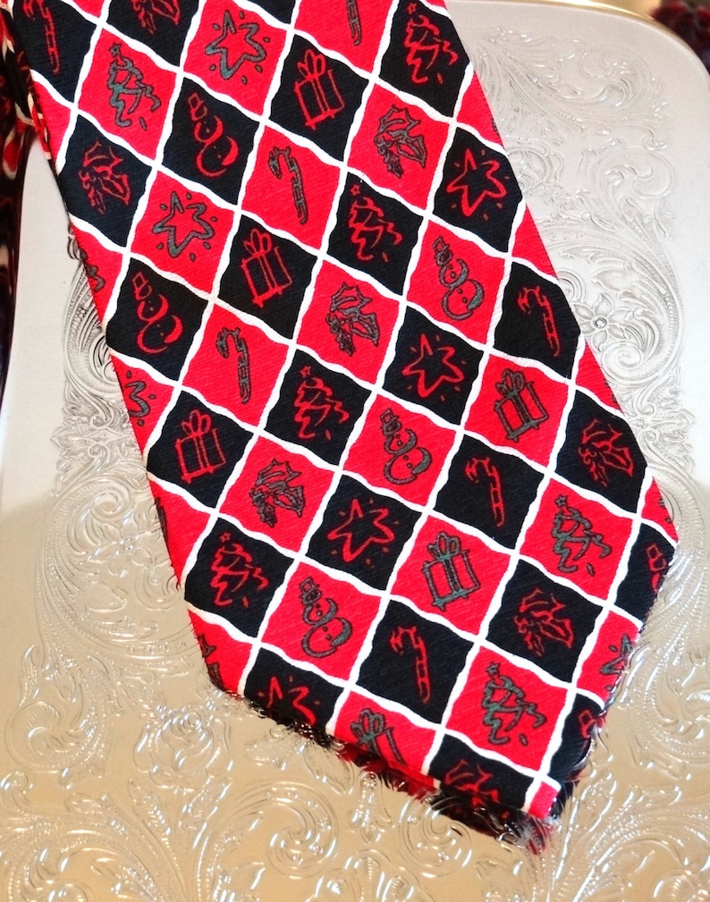 May include: A red and black patterned tie with a Christmas theme. The tie features a repeating pattern of Christmas trees, stars, snowmen, presents, and candy canes.