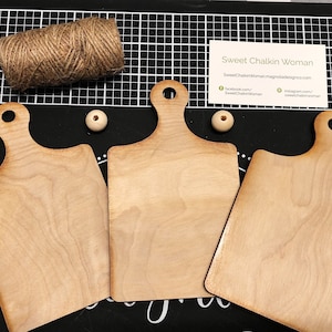 May include: Three unfinished wooden cutting boards with handles. The boards are light brown and have a natural wood grain. The boards are arranged in a row, with the handles facing the viewer.