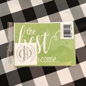 May include: A green stencil with the text "the best is yet to come..." in white cursive lettering. The stencil is packaged in a clear plastic sleeve and includes a white sticker with the text "Magnolia Design Co. Made with Love" in black lettering.