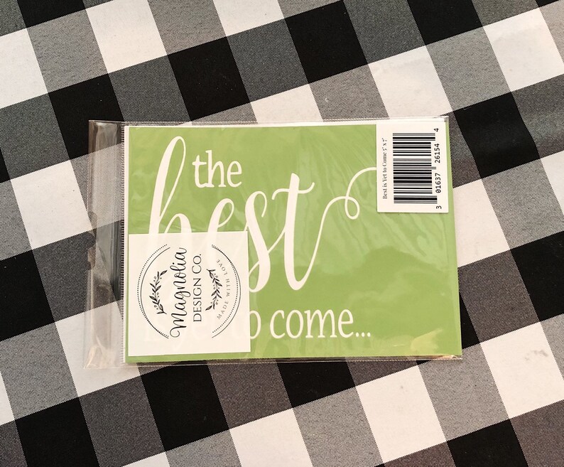 May include: A green stencil with the text "the best is yet to come..." in white cursive lettering. The stencil is packaged in a clear plastic sleeve and includes a white sticker with the text "Magnolia Design Co. Made with Love" in black lettering.