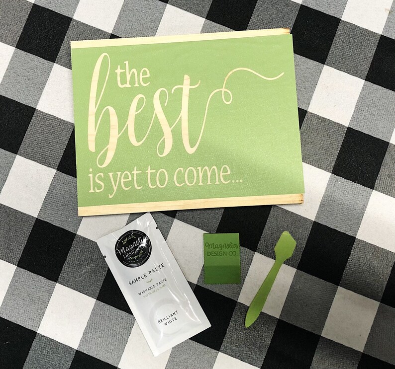 May include: A green wooden sign with the text "the best is yet to come..." in white lettering. A small white packet of sample paste and a green spatula are also pictured.
