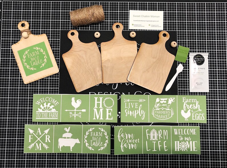 May include: A set of farmhouse-themed craft supplies including three wooden cutting boards, stencils with phrases like "Farm to Table", "Welcome to the Farm", and "Farm Life", and a jar of white paint.