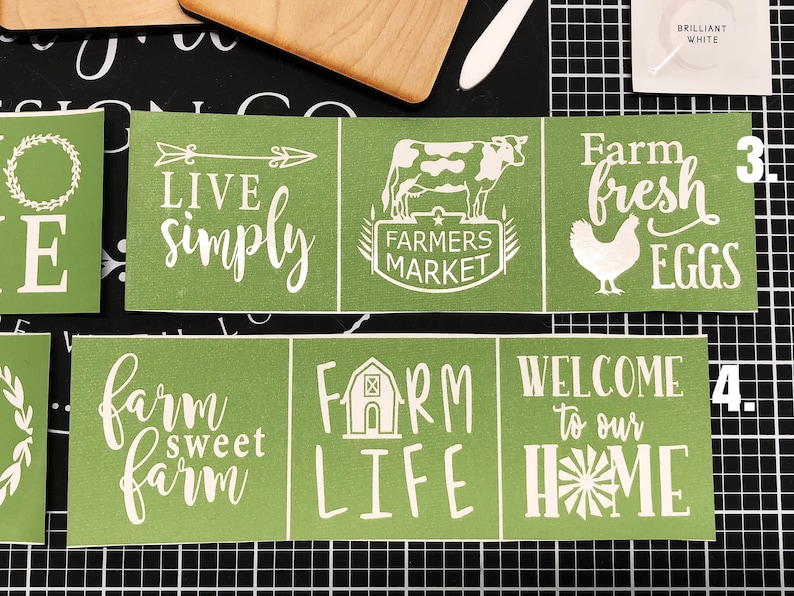 May include: Four green stencils with white vinyl lettering. The stencils feature farm-themed phrases like "Live Simply", "Farmers Market", "Farm Fresh Eggs", "Farm Sweet Farm", "Farm Life", and "Welcome to Our Home".